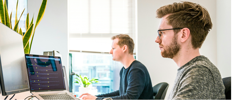Two people working at desks with computers in an office.