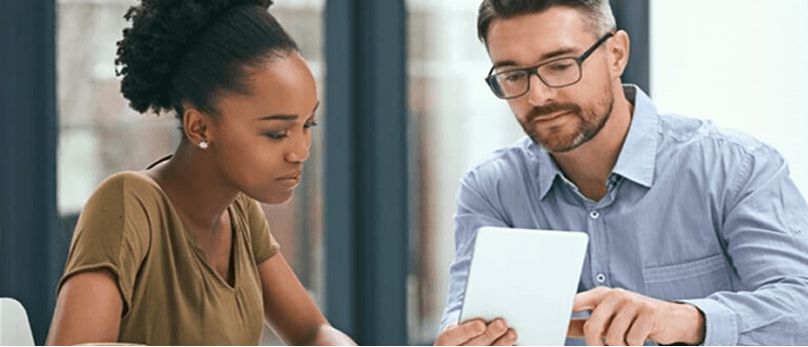 Zwei Personen sitzen an einem Tisch und besprechen etwas auf einem Tablet.