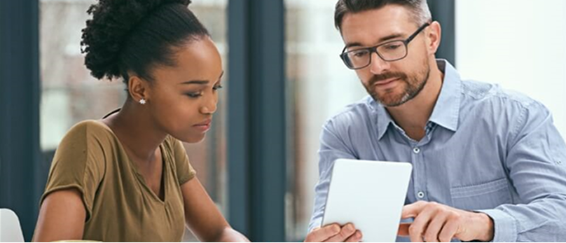 Two people sitting at a table discussing something on a tablet device.