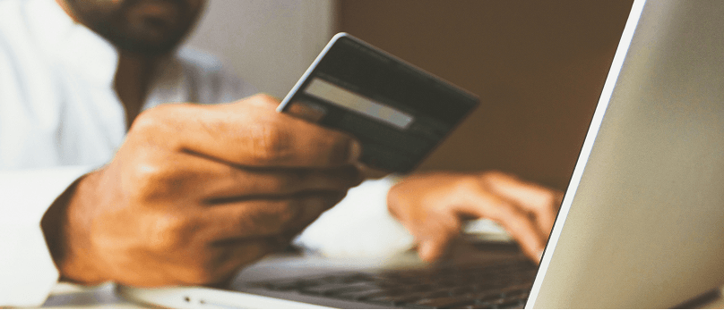 Person, die eine Kreditkarte in der Hand hält, während sie einen Laptop benutzt.