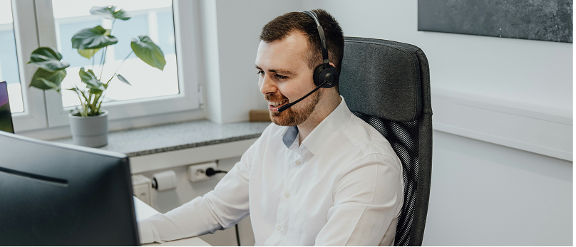 Person wearing a headset and working at a computer in an office.