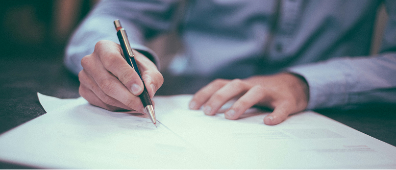 Person writing on a document with a pen at a desk.