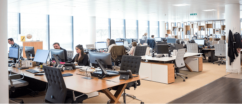 Großraumbüro mit Menschen, die an Schreibtischen und Computern arbeiten.