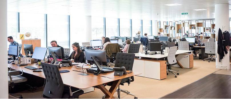 Open-plan office with people working at desks and computers.