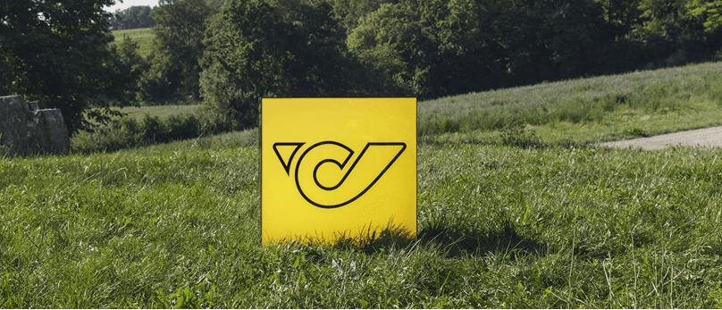 Auf einer Wiese steht ein gelbes Schild mit dem Logo der Österreichischen Post.