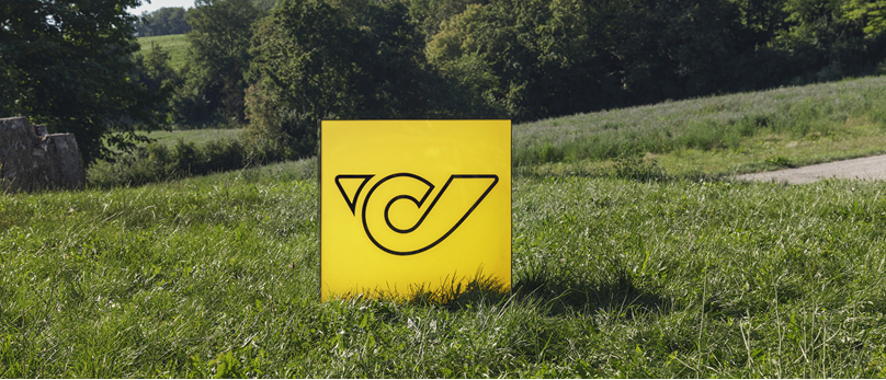 Yellow sign with the Austrian Post logo stands in a grassy field.